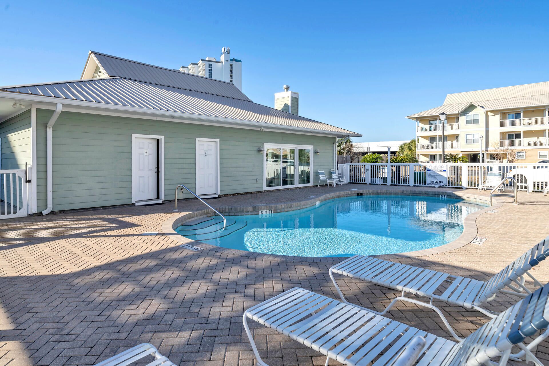 A swimming pool with lounge chairs, a building with a metal roof, and a fenced area.
