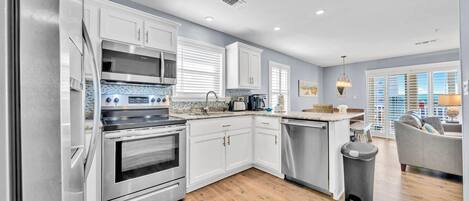 A modern kitchen with stainless steel appliances, white cabinetry, and a wooden floor.