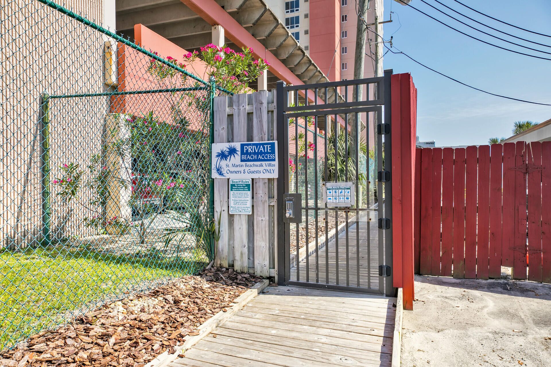 A gated entrance to a private beach area with a wooden deck and a sign indicating beach access for St. Martin Beachwalk Villas owners and guests only.