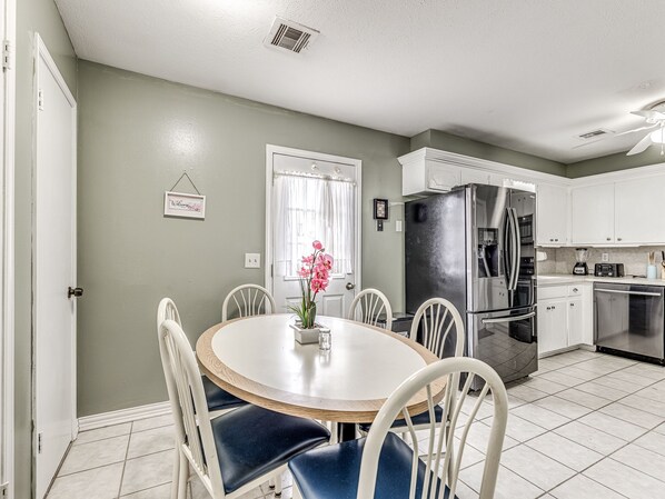 A kitchen with white cabinets, a stainless steel refrigerator, and a dining area with a round table and chairs. -  COZY 3 BEDROOM  HOUSE NEAR WILL ROGERS INTERNATIONAL AIRPORT AND DOWNTOWN OKC (Oklahoma City)