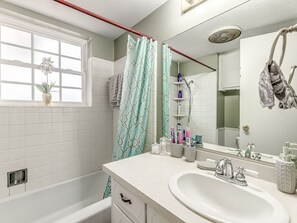 A bathroom with a bathtub, a sink, a mirror, and a window with a plant. -  COZY 3 BEDROOM  HOUSE NEAR WILL ROGERS INTERNATIONAL AIRPORT AND DOWNTOWN OKC (Oklahoma City)