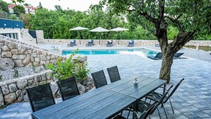 Ein Poolbereich mit Holztisch und -stühlen, einer Steinsäule und Liegestühlen mit Sonnenschirmen.