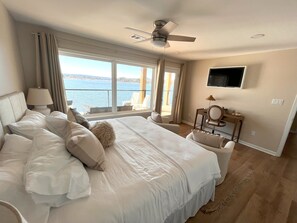 A bedroom with a large bed, a ceiling fan, a TV mounted on the wall, and a view of the water outside. - Luxury Lakeside Home 5BR,4BA, 10+beds. Dock, Kayaks, Fire pit, Hot Tub & more! (Hot Springs)