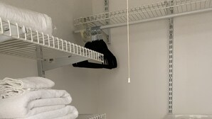 Un armario con estantes blancos, una cesta de ropa blanca y una percha.