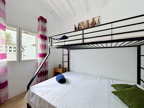 Une chambre avec un lit superposé, une fenêtre, des rideaux et une petite table sur laquelle est posée une plante.
