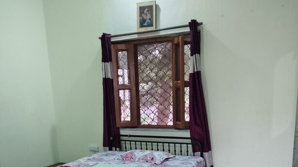Ein Schlafzimmer mit Bett, einem Fenster mit Vorhängen, einem Heizkörper und einem Bild an der Wand.