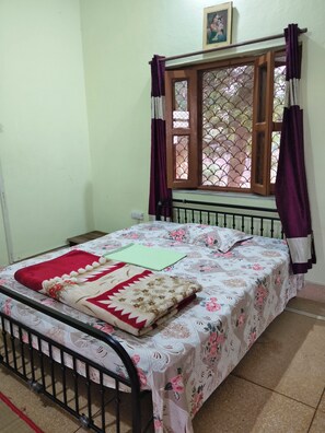 A room with a bed, a window with curtains, a radiator, and a picture on the wall.
