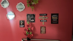 Una pared roja con diversos letreros y decoraciones, incluyendo un letrero con forma de taza de café, un letrero que dice "A vida é dura mas o cafe é forte" y un letrero con un corazón y el texto "O amor está no ar".