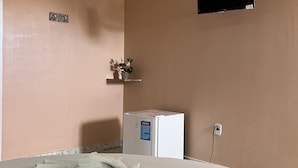 Una habitación con cama, un refrigerador pequeño, un televisor montado en la pared y un enchufe.