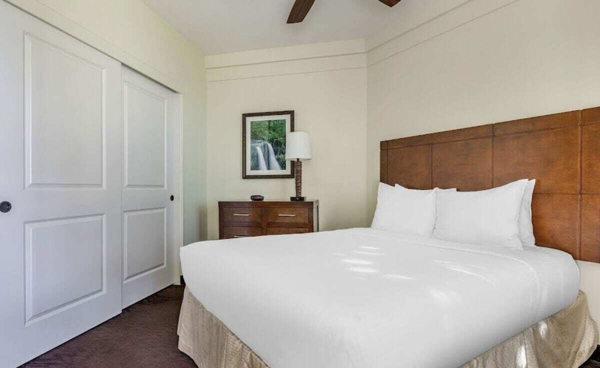 Une chambre d’hôtel avec un grand lit, une tête de lit en bois, une table de chevet avec une lampe et un tableau encadré au mur.