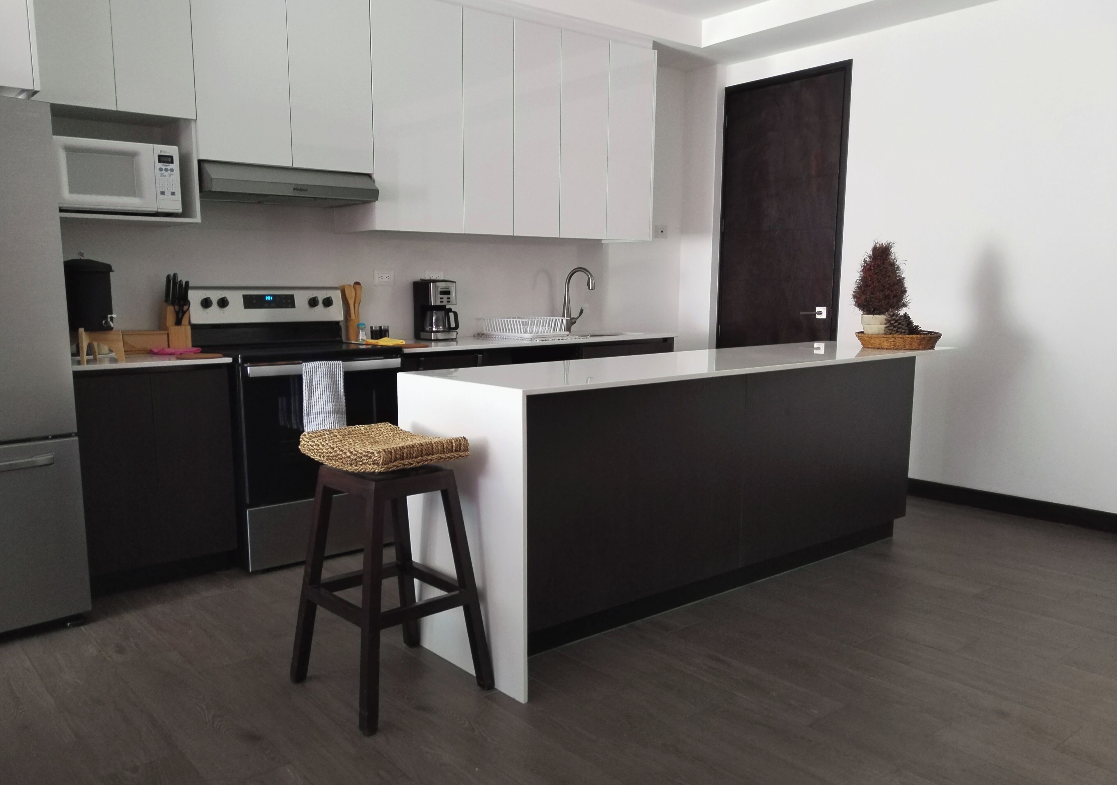 Una cocina moderna con armarios blancos, encimera negra, microondas integrado, estufa y cafetera.