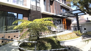 A modern multi-story building with balconies, a covered outdoor area, and a central landscaped garden with a tree. - Suite Zen (Guatemala City)