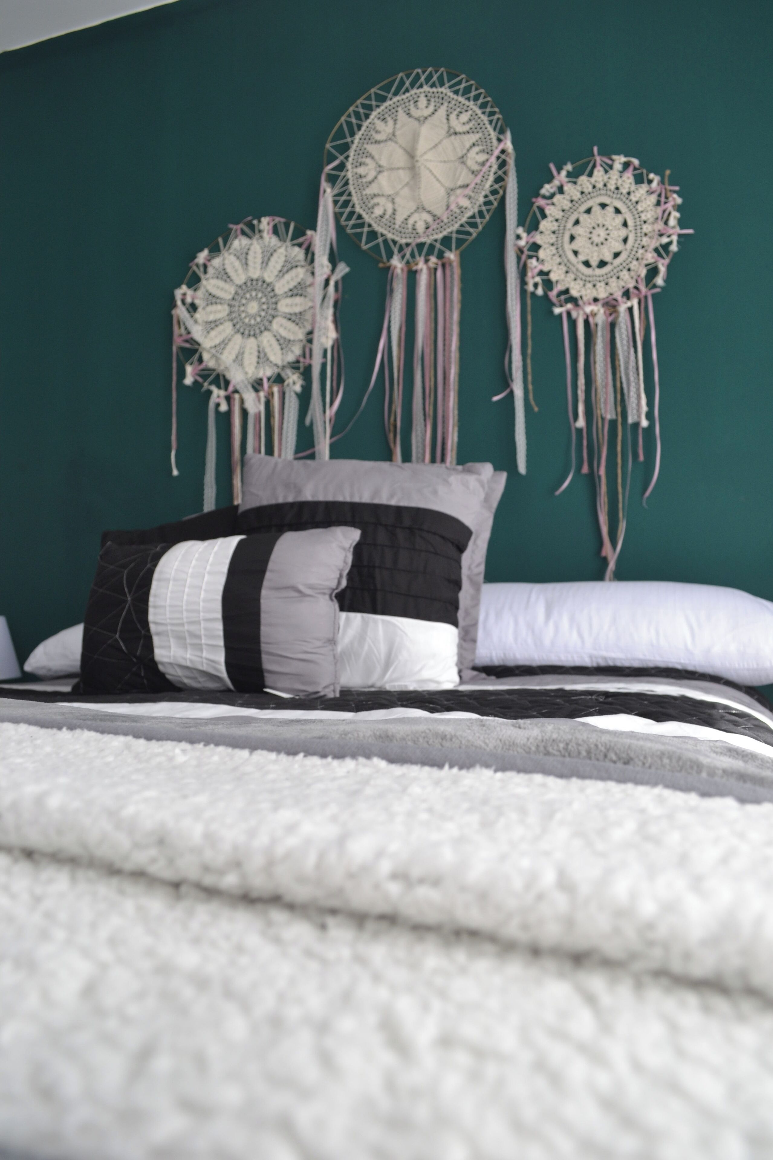 A bed with white and gray bedding, a black and white pillow, and three dreamcatchers on the wall.