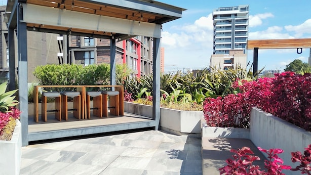 A rooftop terrace with a wooden table and chairs, surrounded by potted plants and flowers. - Suite Zen (Guatemala City)