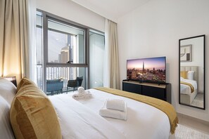 A hotel room with a large bed, a television, a cityscape painting, and a view of the city through a large window.