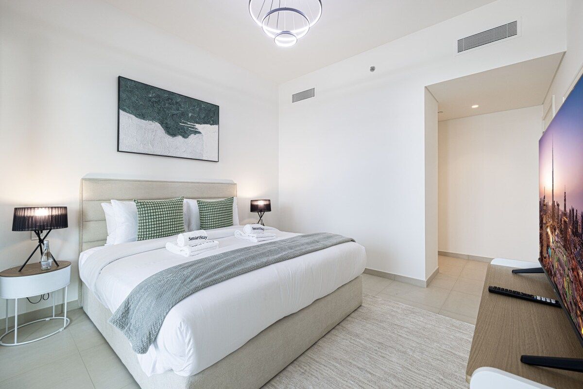 A modern hotel room with a large bed, bedside lamps, a flat-screen TV, and a painting on the wall.