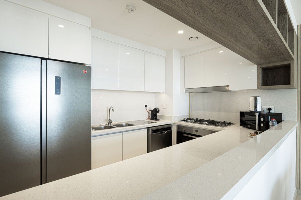 A modern kitchen with stainless steel appliances, white cabinetry, and a granite countertop.