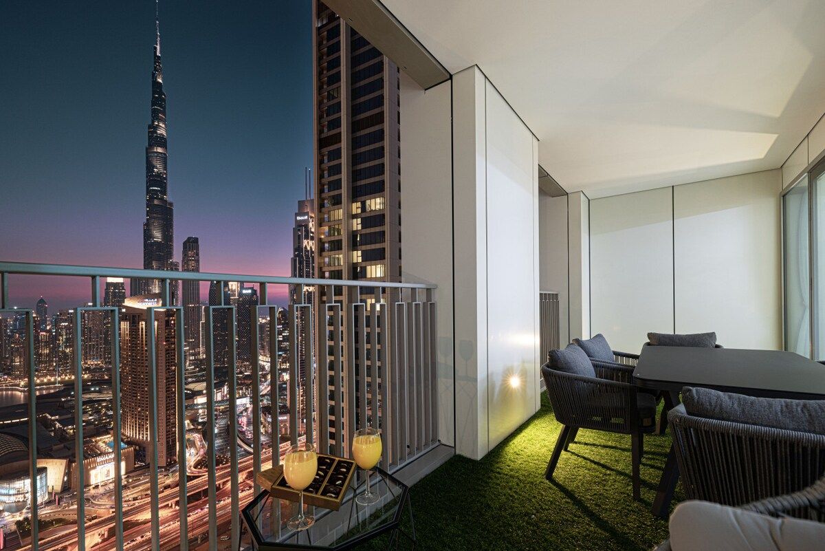 Uma varanda moderna com vista para a cidade, espaço de refeições com mesa e cadeiras, e um canto de estar pequeno com almofadas.