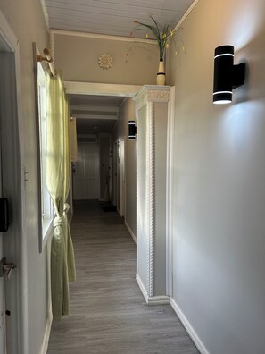 A hallway with a light-colored wooden floor, a white door, and a wall-mounted light fixture. - Carris (Georgetown)