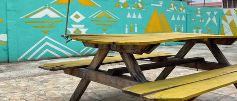 A picnic table with a patterned umbrella in front of a building with geometric wall art.
