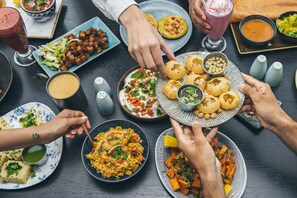 A group of people dining at a table with various dishes, including a plate of fried snacks, a bowl of rice, and a glass of beverage.