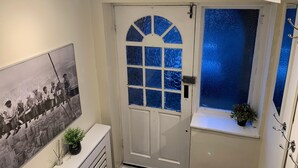 A room with a white door, a window with blue-tinted glass, a framed black and white photo on the wall, and a small plant on the windowsill. - House Sleeps 6 with Garden, Parking (London)