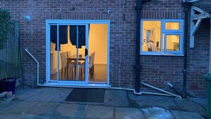 A brick house with a sliding glass door leading to a dining area with a table and chairs. - House Sleeps 6 with Garden, Parking (London)