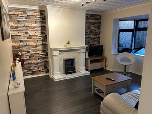 A living room with a fireplace, a television, a window with blinds, and a sofa. - House Sleeps 6 with Garden, Parking (London)