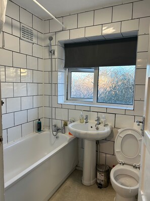 A bathroom with a bathtub, a sink, and a toilet. There is a window with frosted glass and a showerhead above the sink. - House Sleeps 6 with Garden, Parking (London)