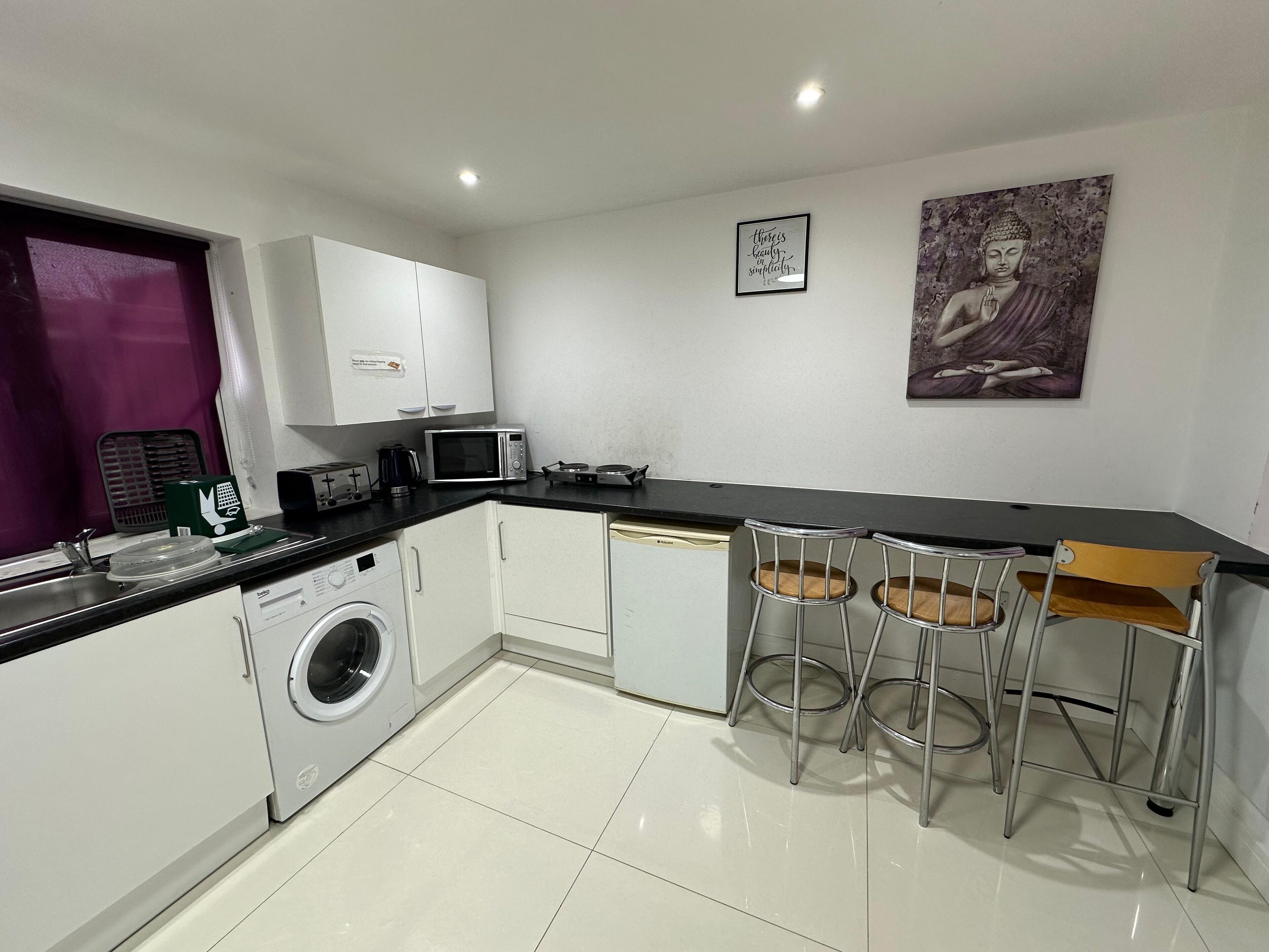 A compact kitchen with a washing machine, microwave, and a small dining area with two stools.
