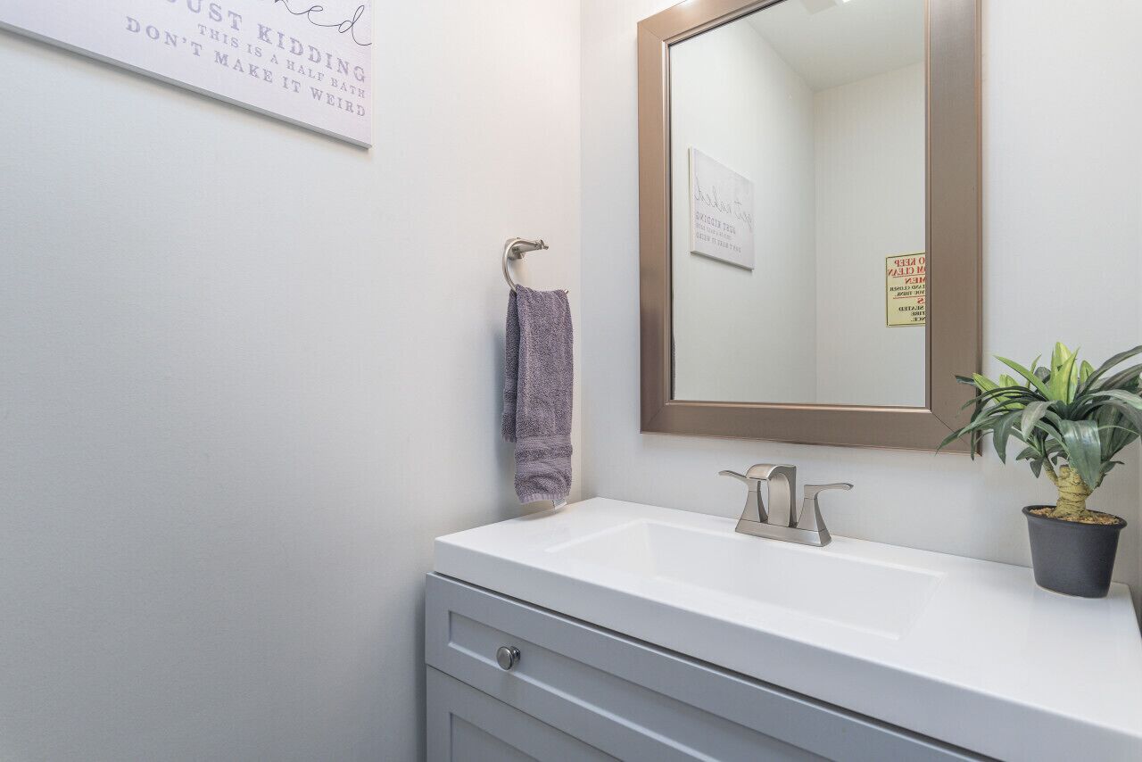 A bathroom with a white sink, a mirror, a towel hanging on a rack, and a potted plant.