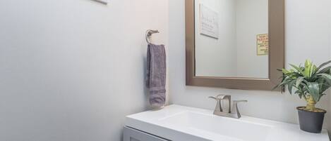 A bathroom with a white sink, a mirror, a towel hanging on a rack, and a potted plant.