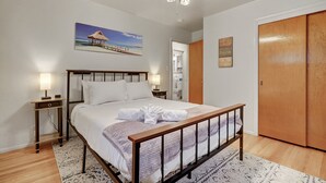 A bedroom with a bed, bedside tables, a ceiling fan, a painting, and a wardrobe.
