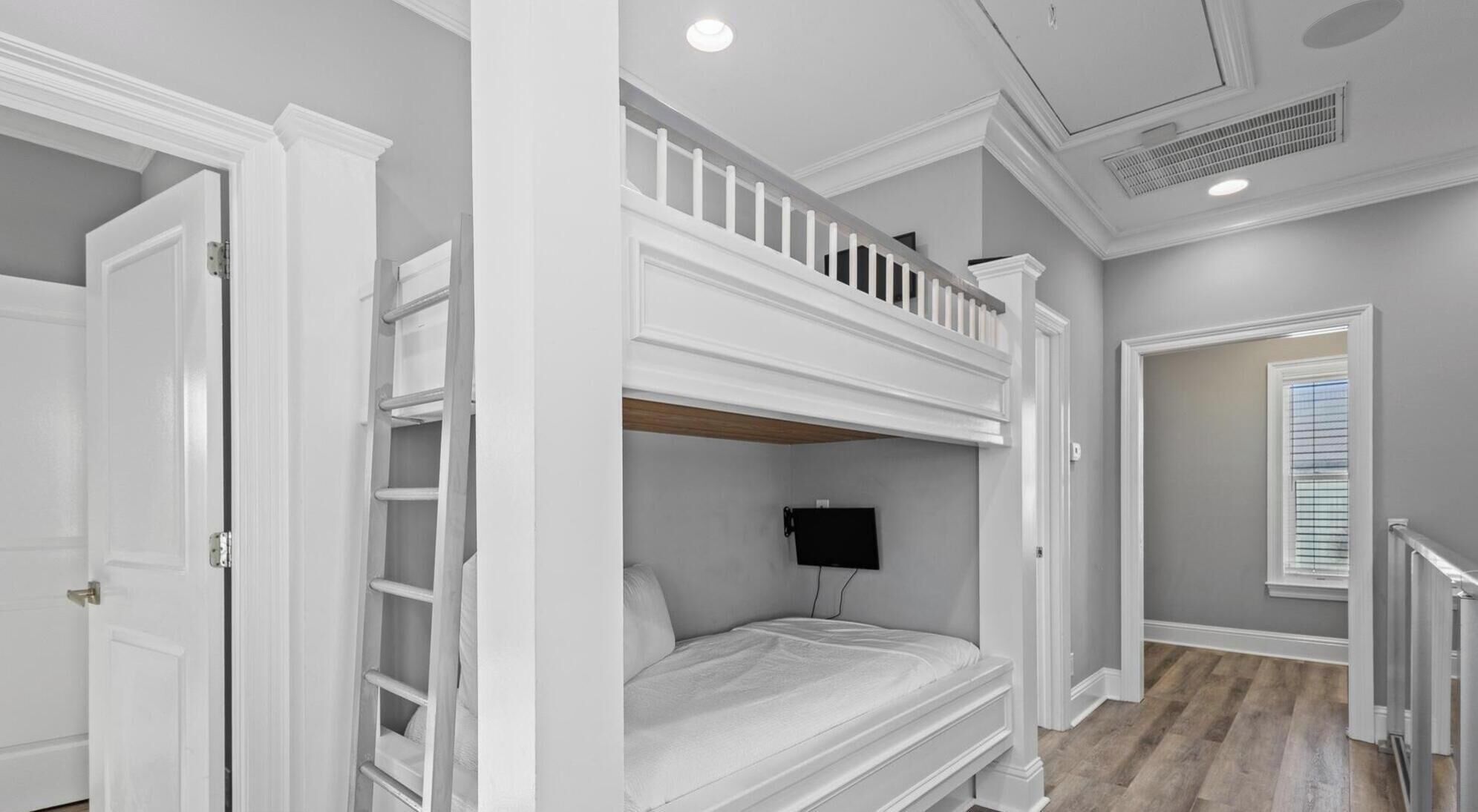 Une chambre avec un lit superposé, une échelle, un téléviseur à écran plat et une fenêtre avec des stores.