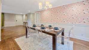 A dining area with a wooden table, clear chairs, and a patterned wall. - Ping-pong | 10-min to NC State | Fire Pit | BBQ (Raleigh)