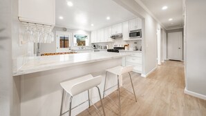 Una cocina moderna con armarios blancos, una isla grande con taburetes de bar y vistas al área de estar.
