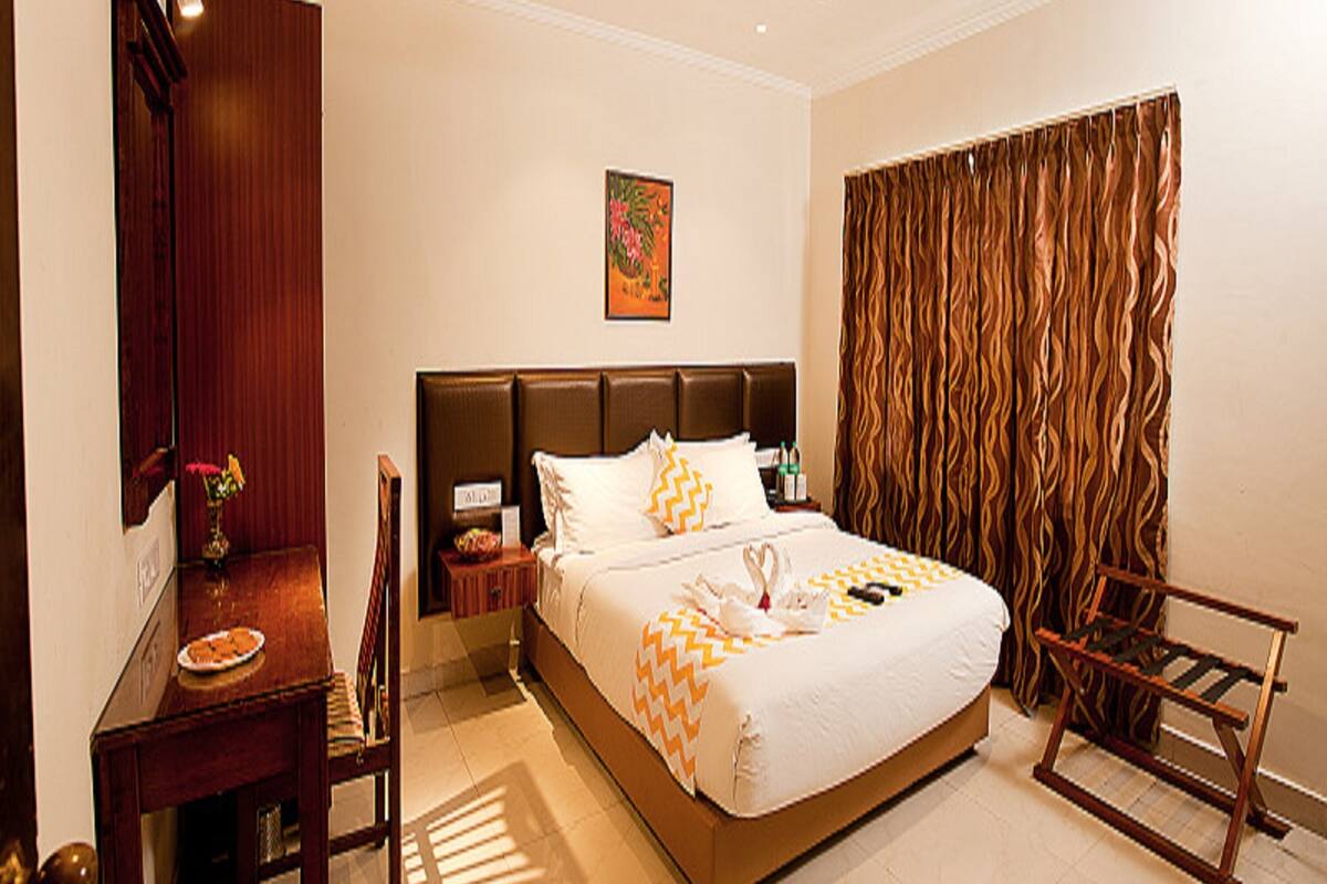 Ein Hotelzimmer mit Bett, Schreibtisch, Stuhl, Nachttisch, Deckenventilator und Vorhang.