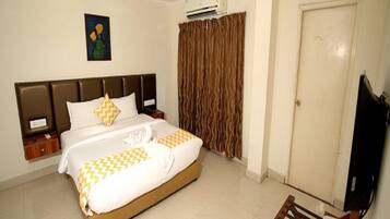 Una habitación de hotel con cama, ventilador de techo, aire acondicionado, televisor y escritorio con silla.