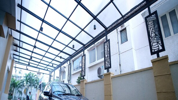 A car parked under a glass-covered walkway with a building in the background. - Blossoms Hotel and Service Apartment (Chennai)