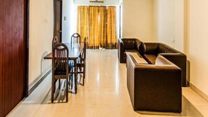 A spacious living area with a dining table and chairs, a sofa, and a large window with curtains. - Blossoms Hotel and Service Apartment (Chennai)