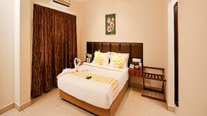 A hotel room with a large bed, a ceiling fan, an air conditioning unit, a wooden wardrobe, a bedside table with a lamp, and a floral wall decoration. - Blossoms Hotel and Service Apartment (Chennai)