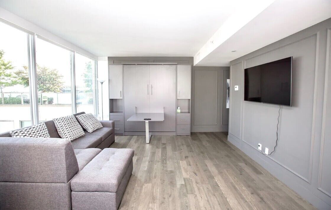 Een moderne woonkamer met een grijze bank, een salontafel en een flatscreen televisie aan de muur.