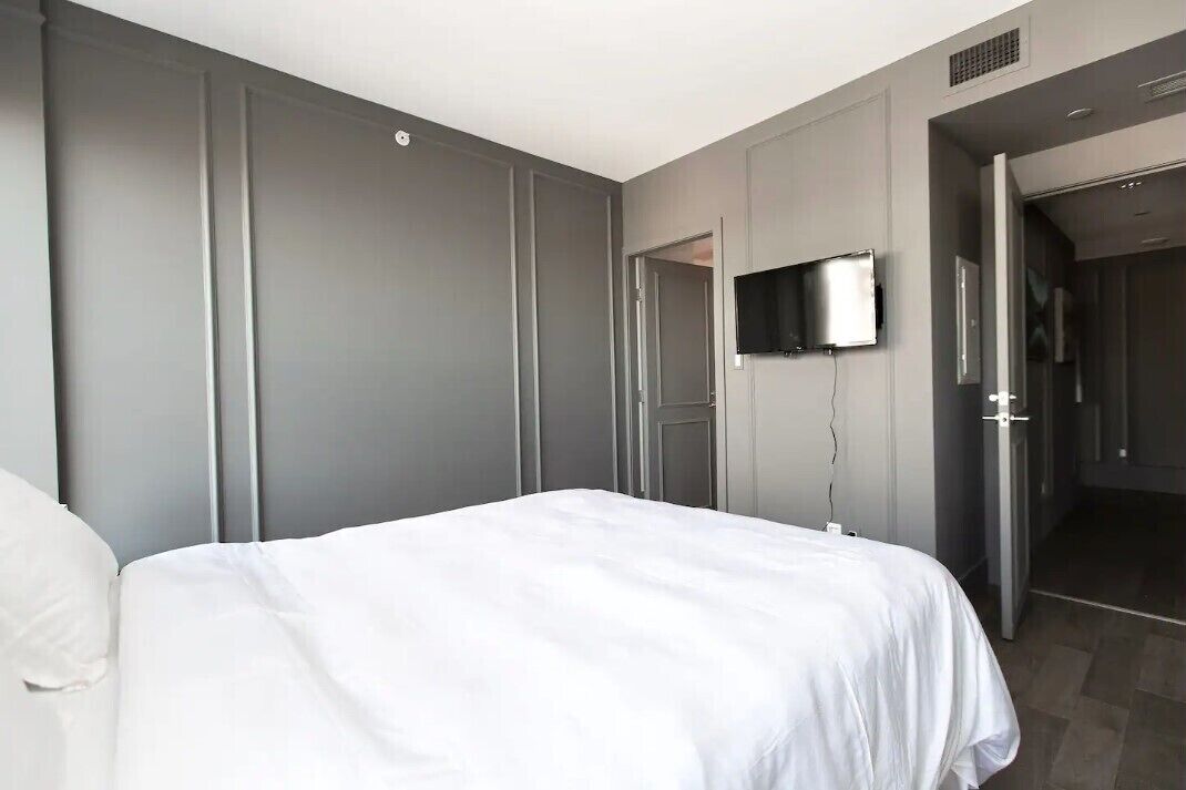 Ein modernes Hotelzimmer mit einem großen Bett, einem flachbildfernseher an der Wand und einer Tür zu einem Badezimmer.
