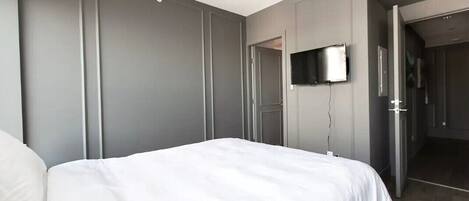 Ein modernes Hotelzimmer mit einem großen Bett, einem flachbildfernseher an der Wand und einer Tür zu einem Badezimmer.