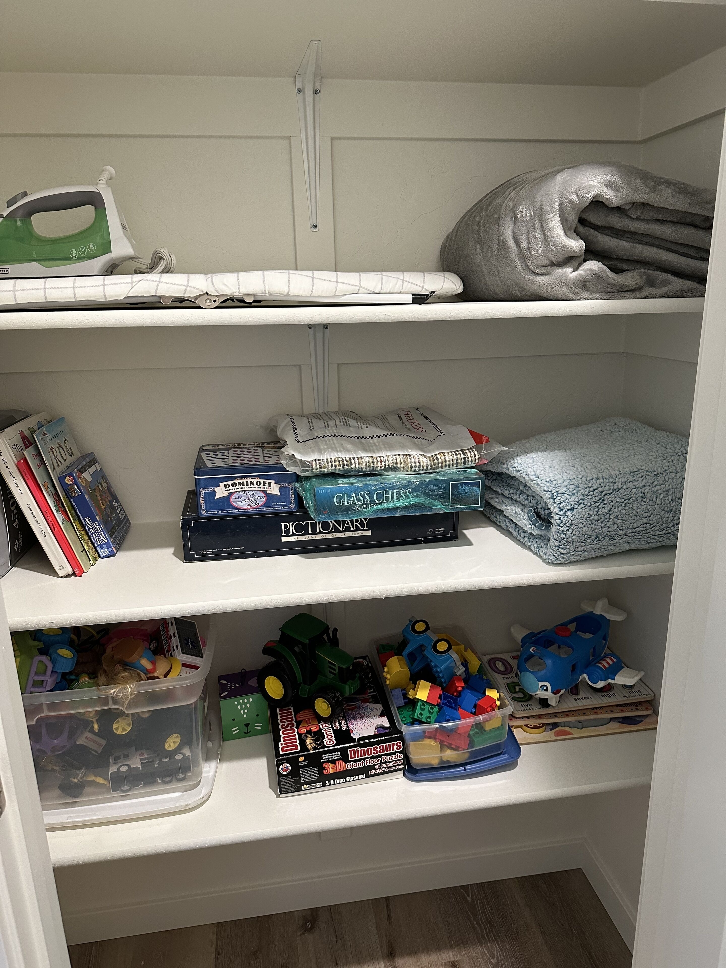Ein Lagerraum mit Regalen, auf denen Bücher, ein grünes Bügeleisen, eine Decke und Kinderspielzeug stehen.