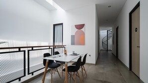 Et moderne, minimalistisk spiseområde med et hvidt bord og sorte stole, et geometrisk kunstværk på væggen, og en trappe der fører op til et andet niveau.