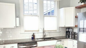 Een moderne keuken met witte kasten, een roestvrijstalen vaatwasser, een houten eettafel en een barkruk.