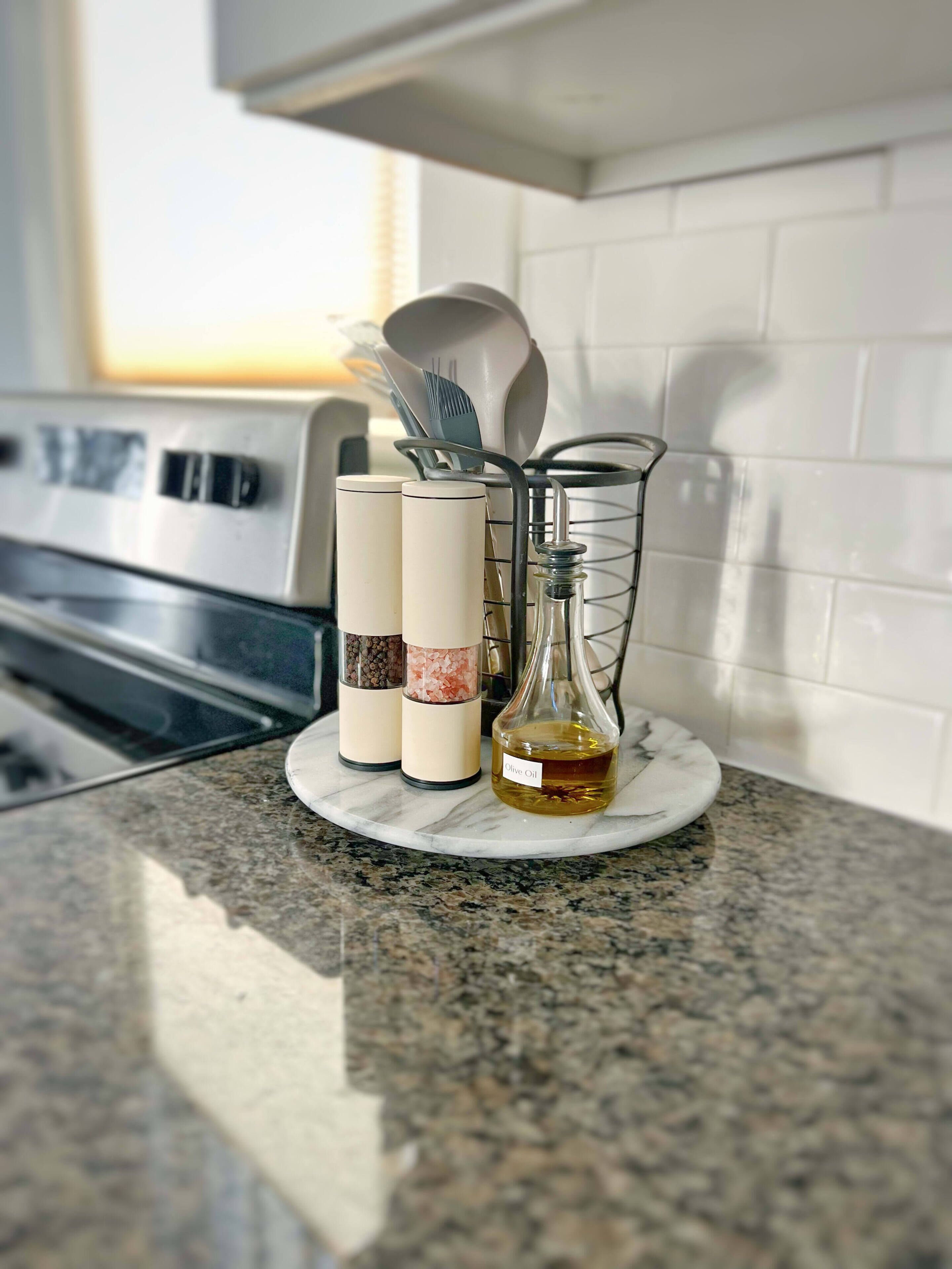 A kitchen counter with a spice rack holding salt and pepper shakers, a glass bottle labeled "Olive Oil," and a metal utensil holder.