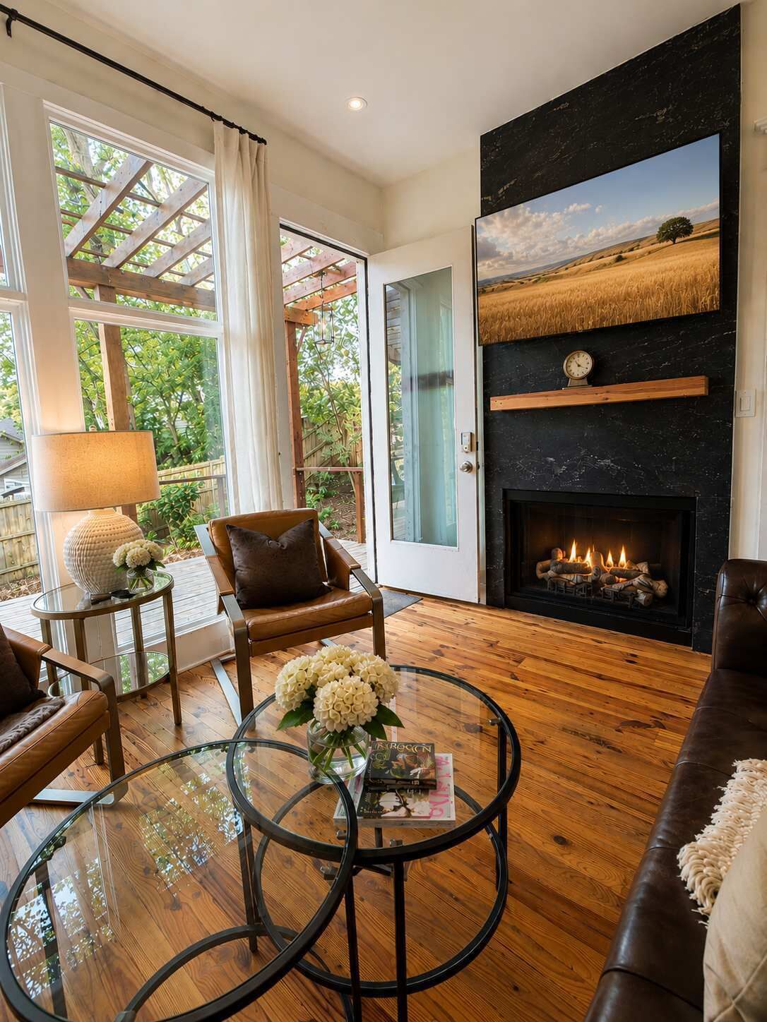 Una sala de estar con chimenea, sofás de cuero, una mesa de centro de vidrio con flores y vistas a través de un ventanal.
