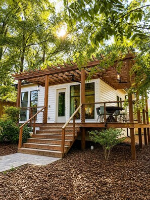 A wooden deck with a staircase leading to a covered porch area, surrounded by trees and a mulched ground. - Designer Garden Home Downtown (Durham)